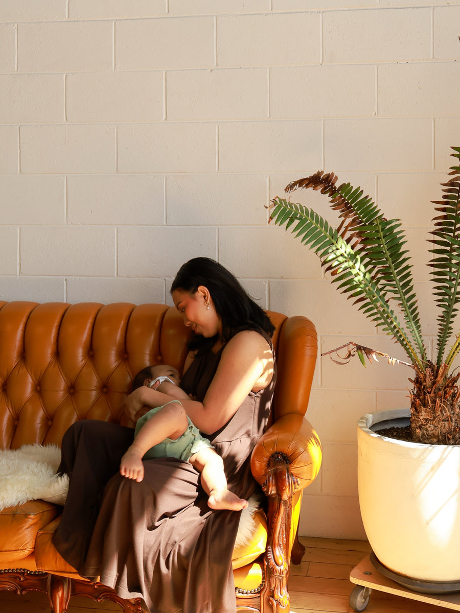 Mum in the Dark Chocolate dress feeding her baby on a leather couch in morning light